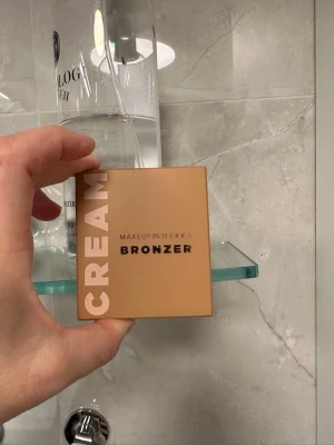 Makeup Mekka Cream Bronzer - Säljer en cream bronzer från Makeup Mekka i en snygg beige fyrkantig dosa med spegel. Bronzern har en varm, naturlig ton som ger huden en solkysst look. Perfekt för att skulptera ansiktet och skapa glow. Smidig att ta med i väskan. Nästan ny! Använd 2 ggr