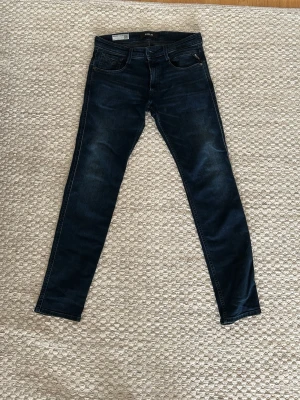 Mörkblå slim fit jeans från Replay - Snygga mörkblå slim fit jeans från Replay med klassisk femficksmodell och subtila slitningar. Jeansen har raka ben och är tillverkade i stretchigt denimtyg för extra komfort. Mycket gott skick. Storlek 31/32