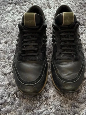 Svarta Valentino Garavani sneakers - Snygga svarta sneakers från Valentino Garavani med coola nitar på sidorna och beige detaljer på tungan. Skorna har en mix av läder och mocka, samt svart sula med beige kant. Såklart 100% äkta! 