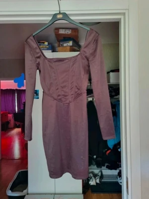 Brun långärmad klänning - Snygg brun klänning med lång ärm och fyrkantig urringning. Klänningen har figurnära passform och markerad midja för en smickrande siluett. Tillverkad i ett mjukt, stretchigt material som känns bekvämt mot huden.