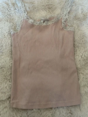 Rosa ribbad linnetopp från h&m  - Säljer en ljusrosa ribbad linnetopp från h&m  med spetsdetaljer runt halsringningen och axelbanden. Toppen är ärmlös och har en smickrande, slim passform. Perfekt att styla med jeans eller kjol för en trendig look. Storlek xxs , pris 10kr