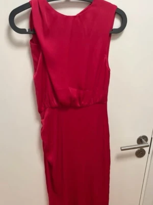 Rosa ärmlös midiklänning - Snygg rosa midiklänning i ett glansigt tyg med rund halsringning och ärmlös design. Klänningen har en markerad midja och dragkedja i ryggen. Perfekt för dig som vill sticka ut med en klassisk och stilren look.