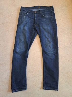 Lee jeans  - Snygga mörkblå slim fit jeans från Lee med klassisk femficksdesign och bruna sömmar. Jeansen har en knappgylf och är tillverkade i stretchigt denimtyg för extra komfort. Perfekta för en avslappnad och trendig look. Storlek W33 L30