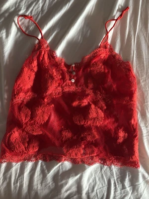 Röd spetslinnetopp med knappar - Snygg röd linnetopp i spets med tunna axelband och dekorativa knappar framtill. 