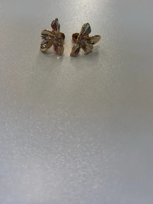 Guldiga blomformade örhängen - Säljer ett par snygga örhängen i guldfärgad metall med blomformad design. 