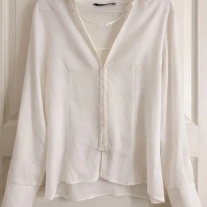 Vit blus med knappar framtill - Vit blus med lång ärm och dolda knappar framtill från Zara. Blusen har en tight pass form som sitter strukturerad till kroppen. Storleken är L men den är väldigt liten i storleken och passar mig perfekt som normalt har storlek S eller M. Användt 1 gång.