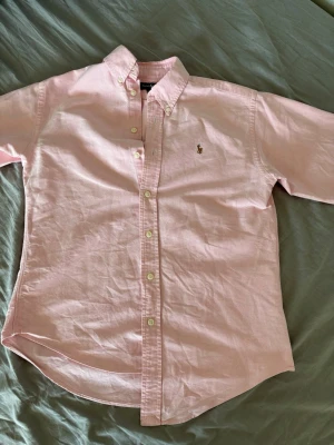 Rosa skjorta från Ralph Lauren - Stilren rosa skjorta från Ralph Lauren med klassisk button-down krage. Den är i storlek S men skulle seja att den passar på xs då den är liten i storleken. den är i bra skick. Å  priset kan diskuteras 