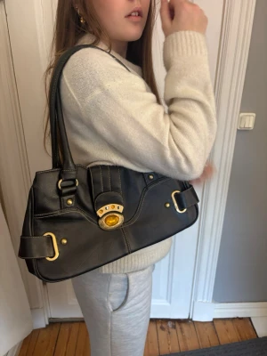 Svart handväska med gulddetaljer - Jätte fin vintage väska med lite till nästan inga spår av användning, däremot saknas det två stenarna knäppet:/ väskan är rymlig med flera fack! Om frågor, skriv privat!🌸