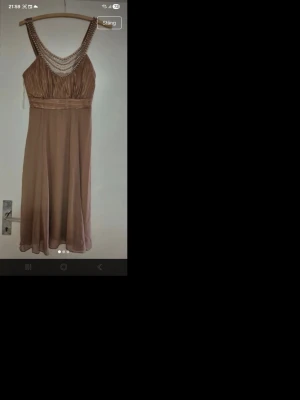 Beige klänning med pärldetaljer - Säljer en elegant beige klänning med v-ringad hals och pärldetaljer runt urringningen. Klänningen har markerad midja och ett mjukt, flytande tyg som ger en fin siluett. Perfekt för dig som vill ha en stilren look.