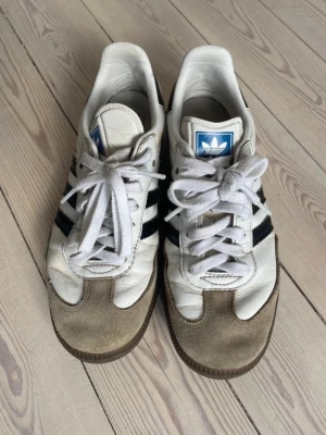 Adidas Samba   - Klassiska Adidas Originals sneakers i vitt läder med beige mockadetaljer och svarta ränder på sidorna.   Köpte de på Vinted för en vecka sedan men säljer redan nu eftersom de var för små  Priset kan diskuteras!!