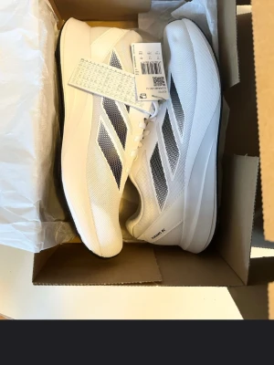 Adidas Duramo RC - Fräscha vita sneakers från Adidas med klassiska svarta ränder på sidorna. Skorna har en låg profil, mesh-ovandel för bra andningsförmåga och en lätt sula som ger skön komfort. Perfekta för dig som gillar stilrena och sportiga sneakers. Det är ganska få nya ute då det inte ens finns kvar på Adidas hemsidan och speciellt denna storlek😊 vid frågor är det bara att ni hör av er🤗
