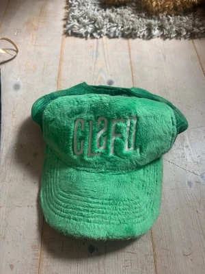 Classfield  - Säljer en grön keps från classified med mjuk plysch framtill och mesh baktill för extra ventilation. Kepsen har broderad vit logga framtill och justerbar snapback. Perfekt för dig som vill ha en unik och trendig accessoar.