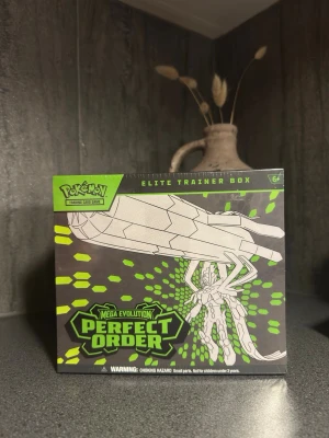 Pokémon Elite Trainer Box Perfect Order - Säljer en Pokémon Elite Trainer Box Mega Evolution Perfect Order. Boxen är svart med gröna och vita detaljer och innehåller booster packs, samlarkort, tärningar och tillbehör för Pokémon Trading Card Game. Perfekt för dig som vill ta ditt kortspelande till nästa nivå.