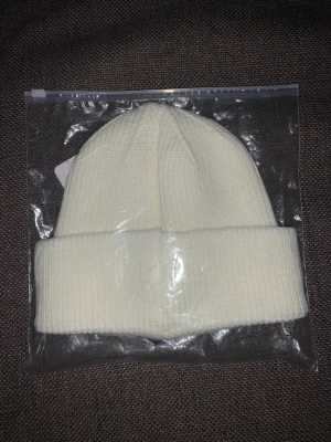 Vit ribbstickad mössa från C.P. Company - Säljer en stilren vit ribbstickad mössa från C.P. Company. Mössan har en bred uppvikt kant och är tillverkad i mjukt material som håller dig varm. Perfekt accessoar för kalla dagar och enkel att matcha med olika outfits.