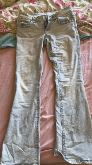 Ljusblå bootcut jeans - Säljer ett par ljusblå bootcut jeans med klassiska fem fickor och snygga detaljer på bakfickorna. Jeansen har en knapp och dragkedja framtill och är tillverkade i denim. Perfekt för dig som gillar en avslappnad och trendig look.
