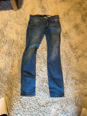 Blå slim fit jeans från Replay - Säljer ett par klassiska blå slim fit jeans från Replay  med fem fickor och snygga sömmar. Jeansen har en normal midja och raka ben, tillverkade i ett mjukt denimtyg som ger en skön passform. Perfekta för en avslappnad och trendig look.
