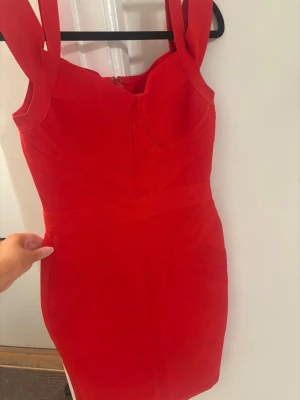 Röd bandage klänning - Snygg röd kort klänning med breda axelband och figurnära passform. Klänningen har markerad midja och dragkedja bak. Perfekt för dig som vill sticka ut med en enkel men stilren look.