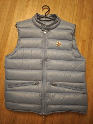 Moncler Gui Väst. Nyskick. Storlek 2 - Moncler Gui Down Vest. I den otroligt populära och eftertraktade färgen light blue. Västen är använd få gånger och i perfekt skick eftersom den är något stor på mig, så jag har köpt en mindre istället. Alla tags, qr kod osv finns. Storlek 2 som motsvarar Small och Medium