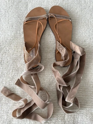Beige sammetsandaler från Valentino - Snygga sandaler från Valentino i beige sammet med långa band att knyta runt vristen. Platta sulor och minimalistisk design med tunna remmar framtill. Perfekta för en trendig och avslappnad look.