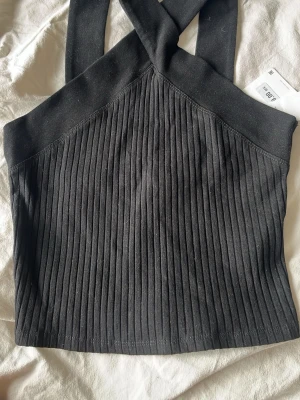 Svart ribbad croppad linnetopp - Säljer en svart croppad linnetopp från Zara med breda axelband. Toppen är ribbad och har en stilren, modern look som passar perfekt till jeans eller kjol. Materialet är mjukt och stretchigt, vilket gör den bekväm att bära.