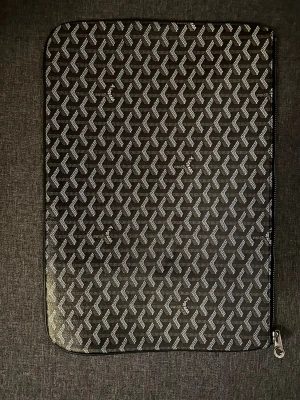 Svart datorfodral med mönster - Snyggt svart datorfodral med vitt grafiskt mönster och dragkedja längs kanten. Fodralet har en rektangulär form och är gjort i ett glansigt material som ger en exklusiv känsla. Perfekt för att skydda din laptop i väskan.