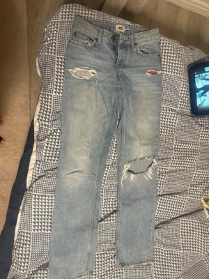 Ljusblå slitna jeans från 157 - Säljer ett par ljusblå jeans med slitningar och hål på både fram- och baksida. Jeansen har klassisk femficksmodell, raka ben och en avslappnad passform. Perfekta för en trendig och avslappnad stil.