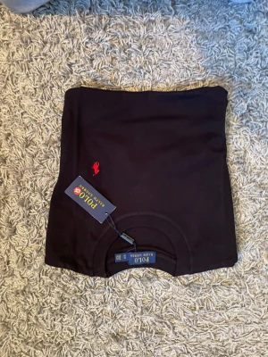 2 st Polo Ralph Lauren - Snygg svart t-shirt från Polo Ralph Lauren med klassisk röd logga broderad på bröstet. T-shirten har rund hals och är tillverkad i mjuk bomull som känns skön mot huden. Perfekt basplagg för en clean och stilren look.