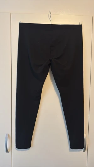 Svarta basic leggings med hög midja - Säljer ett par svarta leggings med hög midja och smal passform. De är helt släta utan synliga loggor eller detaljer och har stretchigt material som sitter tajt längs benen. Perfekta för dig som gillar en clean och enkel stil.