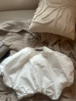 Vit puffig croppad blus  - Supersnygg vit blus  med puffiga korta ärmar och croppad passform. Tillverkad i bomull för en luftig känsla. Perfekt till jeans eller kjol för en trendig look. Elastisk nederkant ger en cool ballong-effekt. strl L passar S/M