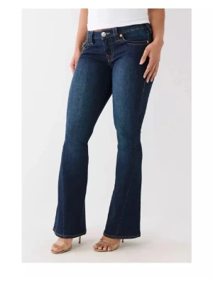Mörkblå True Religion Jeans  - Snygga mörkblå bootcut jeans från True Religion med kontrastsömmar och fina fickdetaljer bak. Klassisk femficksmodell med låg midja och bootcut vid slutet. Perfekta för dig som inte gillar basic jeans.
