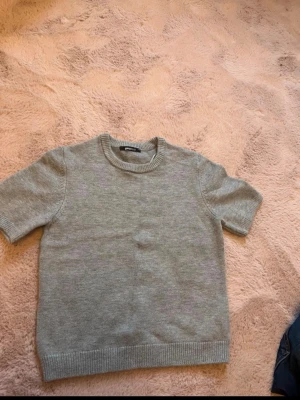 Grå stickad topp från Gina Tricot - Säljer en enkel och stilren grå stickad topp från Gina Tricot. Toppen har korta ärmar, rund halsringning och ribbade kanter. Perfekt att matcha med jeans eller kjol för en clean look. Varan har inte använts många gånger, den är väldigt bekvämt och fin. 