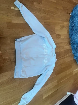 Ljusblå sweatshirt med tryck - Ljusblå sweatshirt med rund hals och ribbade muddar. Tryck i vitt framtill med texten 'California'. Avslappnad passform och mjukt material, perfekt för en chill look.