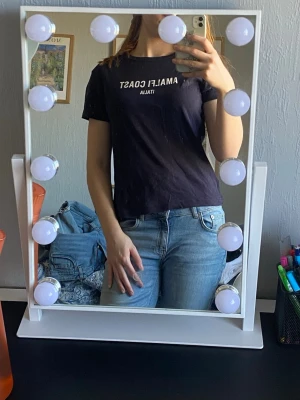 Mörkblå t-shirt med tryck - Säljer en mörkblå t-shirt med texten 'AMALFI COAST ITALIA' tryckt på bröstet. T-shirten har klassisk passform, rund hals och korta ärmar. Perfekt till jeans eller shorts för en enkel och snygg look. 