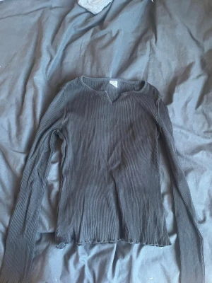 Svart ribbad långärmad topp - Säljer en svart ribbad långärmad topp med v-ringad hals. Toppen har en figurnära passform och vågig kant nertill. Perfekt att styla med jeans eller kjol för en enkel men snygg look. (Klicka ej köp nu) kontakta gärna och Swish går ❤️