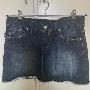 Jeanskjol från Victoria Beckham  - Mörkblå jeanskjol från Victoria Beckham med  snygga guldbroderade kronor på bakfickorna.  Använd endast 1 gång 