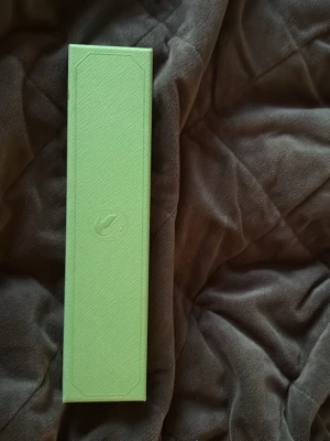 Grön smyckesask från Swarovski - Snygg och stilren smyckesask från Swarovski i ljusgrönt med diskret logga på locket. Perfekt för att förvara armband eller halsband. Asken har en elegant och avlång form och är tillverkad i hård kartong med mjuk insida.