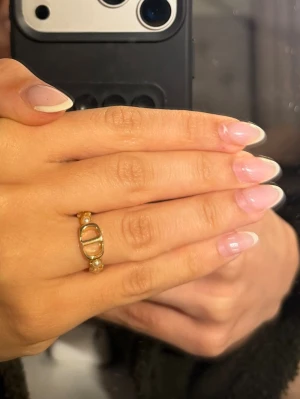 Guldfärgad ring med pärlor och stjärna - Trendig guldfärgad ring med små vita pärlor och en dekorativ stjärna. Ringen har en unik design med en oval detalj framtill och pärlor längs bandet. Perfekt accessoar för att lyfta din stil.