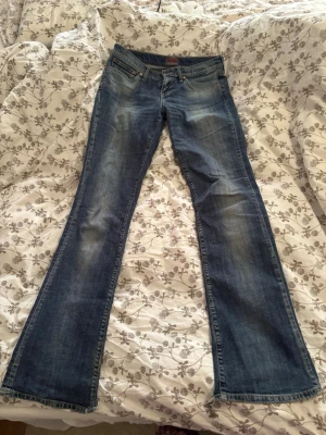 Lågmidjade bootcut jeans - Säljer ett par blå bootcut jeans med låg midja. Jeansen har klassisk femficksmodell och en snygg tvätt med ljusare partier på låren. Perfekta för dig som gillar en avslappnad och trendig stil. De är lite slitna längst ner de de har varit lite för långa på mig men annars är de i jättebra skick och de är as snygga. Storleken är size 30/ length 34. Mått: midja rakt över 38,5cm, innerbenslängd 83cm och innersöm (från topp till sömmen mellan benen) är 21cm.