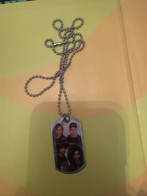 Halsband med Tokio hotel i rostfritt stål - Säljer ett halsband med kulkedja i silverfärg och en rektangulär dog tag-berlock med ett tryckt foto. Halsbandet har en enkel och stilren design som passar till många olika stilar. Med Tokio hotell. Helt nytt i rostfritt stål.