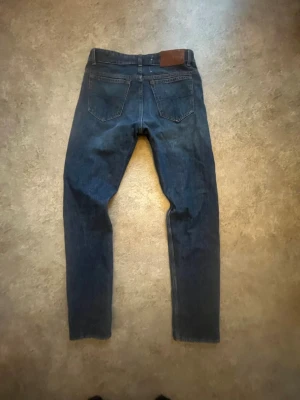 Tiger of sweden jeans - Säljer ett par klassiska mörkblå jeans från tiger of Sweden. Jeansen har raka ben, två bakfickor och detaljer i kopparfärgade nitar. Tillverkade i slitstarkt denimtyg med en snygg läderpatch i midjan. Perfekta för dig som gillar tidlös stil.