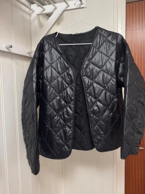 Svart quiltad cardiganjacka - SÖKER!!! Söker denna jacka i storlek XS. Har denna i s och är intresserad av ett byte! Så köp EJ men hör av dig om du har denna i storlek XS och vill byta till en S😊😊Stilren svart quiltad cardiganjacka med rund halsringning och lång ärm. Jackan har ett glansigt yttertyg i syntetmaterial och ett rutmönstrat, vadderat utförande. Perfekt att slänga över en hoodie eller t-shirt för en cool lager-på-lager-look.