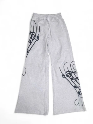 Grå mjukisbyxor med svart print - Säljer ett par grå mjukisbyxor med unikt svart grafiskt tryck på båda benen. Byxorna har breda ben, resår i midjan och är tillverkade i mjukt sweatshirtmaterial. Perfekta för en chill och trendig look.