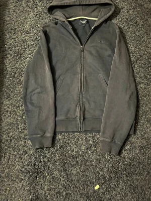 Mörkblå bondelid zip - En mörkblåbondelid  hoodie med dragkedja och huva. Modellen har två fickor framtill och ribbade muddar vid ärmar och nederkant. Perfekt för en avslappnad stil och funkar året runt.