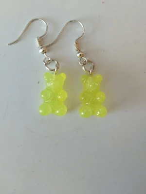 Neongula nallebjörnsörhängen - Unika örhängen med neongula nallebjörnar i plast. Hängande modell med silvriga krokar. Perfekta för dig som vill sticka ut med lekfulla accessoarer och älskar färg. Nallebjörnarna har en glittrig finish som ger extra wow-effekt.