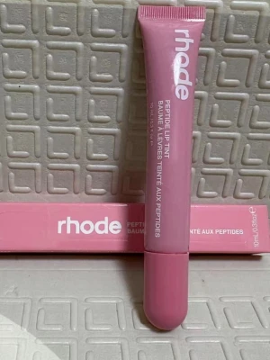 Rhode Peptide Lip Tint rosa läppbalsam - Säljer ett Peptide Lip Tint läppbalsam från Rhode i en snygg rosa nyans. Tuben är smidig och lätt att ta med i väskan. Perfekt för dig som vill ha återfuktade läppar med en hint av färg. Innehåller peptider för extra vård.
