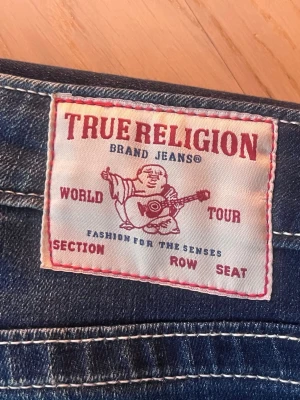 True Religion blå jeans - Säljer ett par blå low waist bootcut jeans från True Religion med den ikoniska loggan på bakfickan. Knappt använda. Galet bra pris 💸Hör gärna av dig oavsett fråga💕🥰🫶🏼