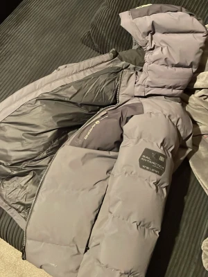 Sail racing antartica jacka - Säljer en grå pufferjacka från sail racing med huva och dragkedja. Säljer jacka eftersom den har blivit för liten. Jackan har en bröstficka med dragkedja och patch på ärmen. Perfekt för kalla dagar och riktigt snygg streetstil.