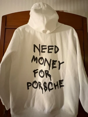 Vit hoodie med tryck 'Need Money for Porsche' - Nu säljer jag en vit hoodie med stor svart text på ryggen: 'NEED MONEY FOR PORSCHE'. Klassisk passform med huva och ribbade muddar. Perfekt för dig som gillar streetwear och vill sticka ut med ett statement-plagg. Hoodien är storlek S. Priset går att diskuteras som vanligt! 😁😉🤝