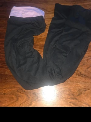 Svarta leggings med lila midja - Säljer ett par svarta leggings med bred lila midja. De är stretchiga och mjuka, perfekta för en avslappnad stil. Passar till många olika outfits och är riktigt bekväma att bära hela dagen.