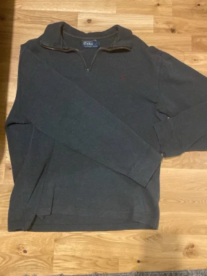 Skogsgrön stickad tröja Polo Ralph Lauren - Skogsgrön stickad tröja från Polo Ralph Lauren med lång ärm och half zip-dragkedja. Klassisk design med liten röd logga broderad på bröstet. Perfekt till chill vardagsstil och enkel att matcha med jeans eller chinos.